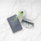 Stone Gray Showerspecs resting on a counter near a book. 
