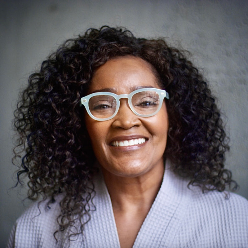 A woman wearing Misty Green Showerspecs reading glasses.