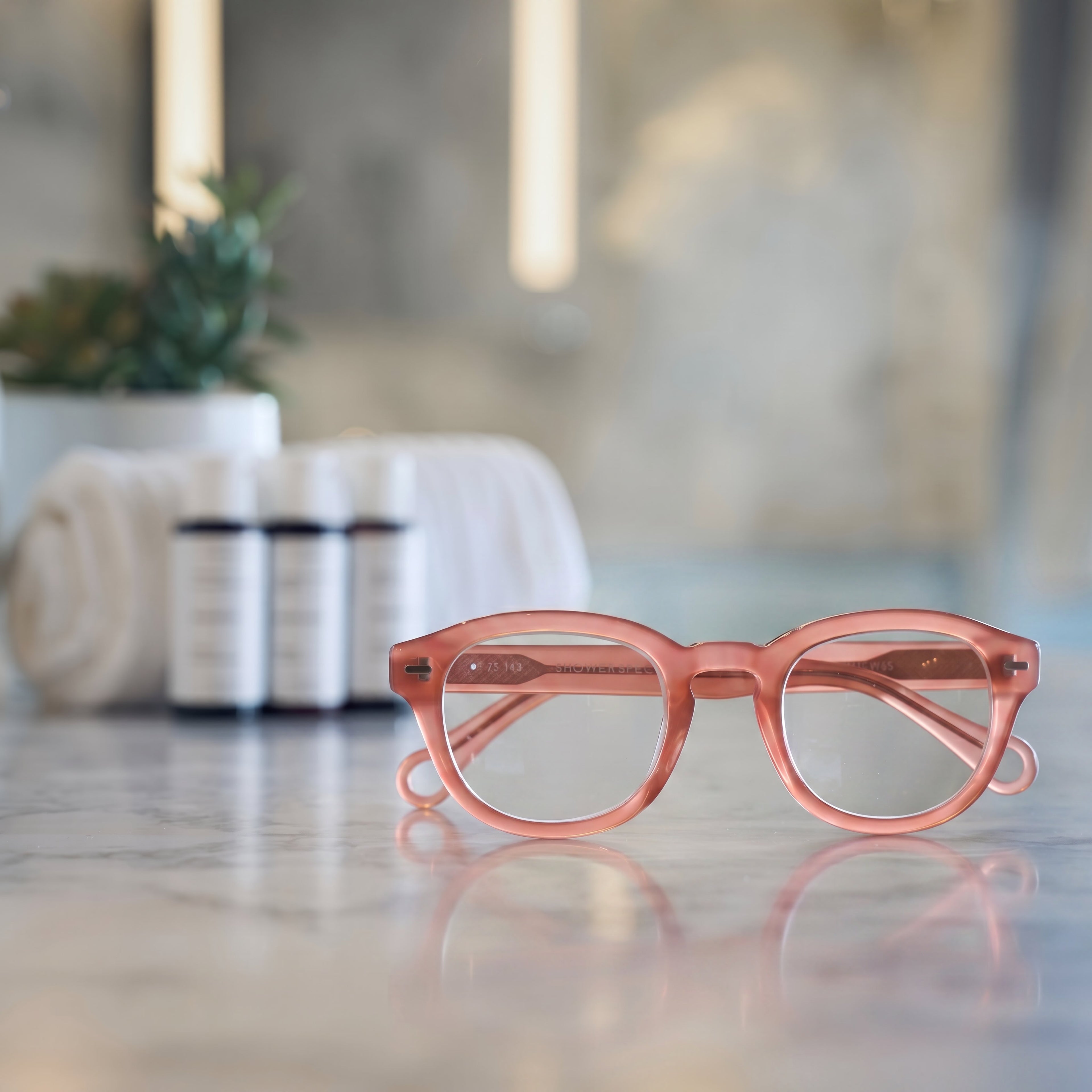 Warm Coral Showerspecs reading glasses on a bathroom countertop.