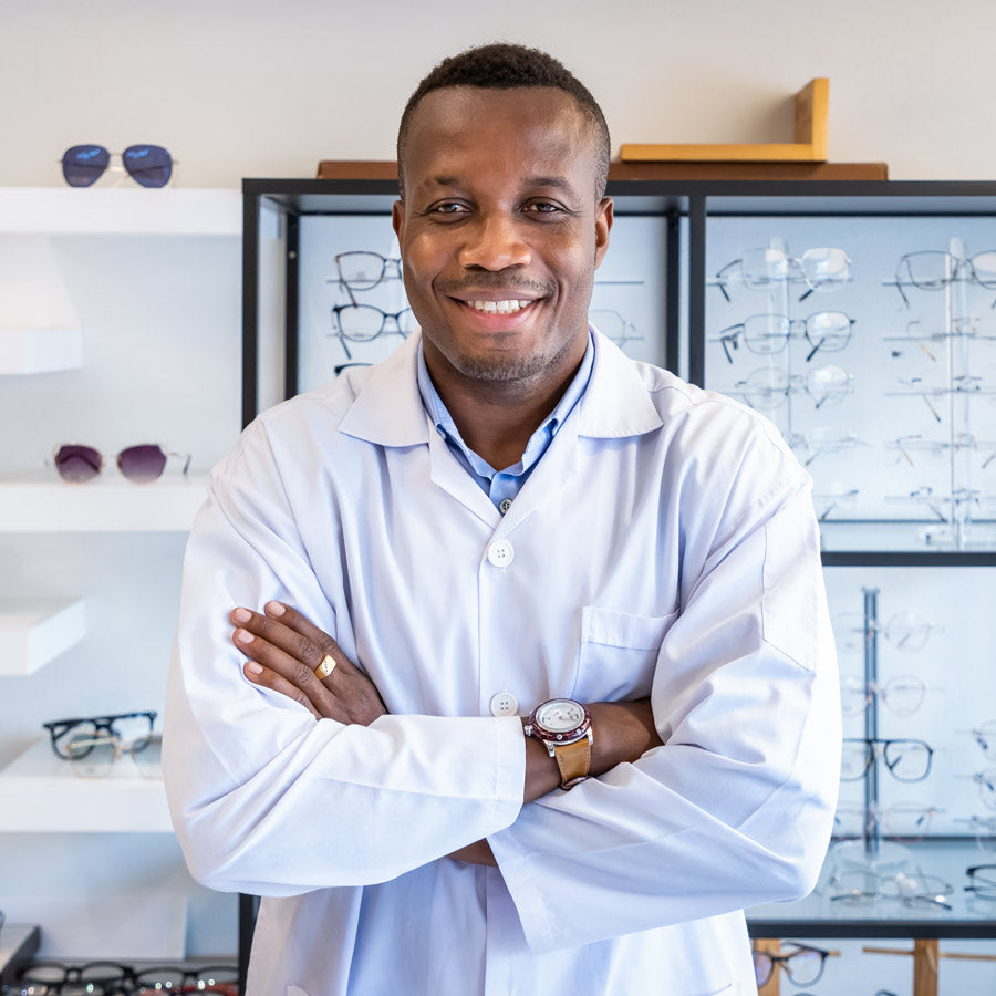 Optometrist smiling in an optical shop with eyeglass displays in the background.
