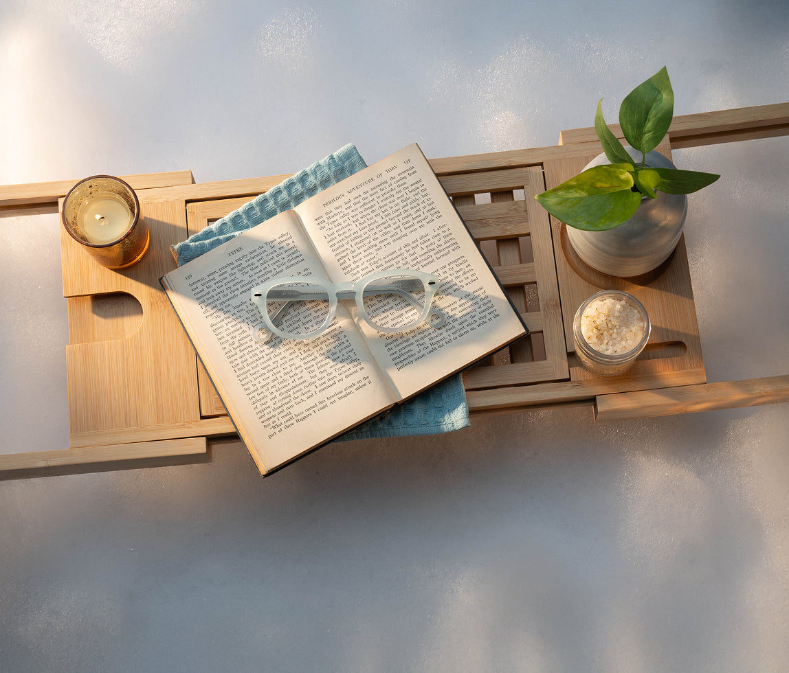 Crystal Clear Showerspecs reading glasses on an open book on a tray over the bathtub.